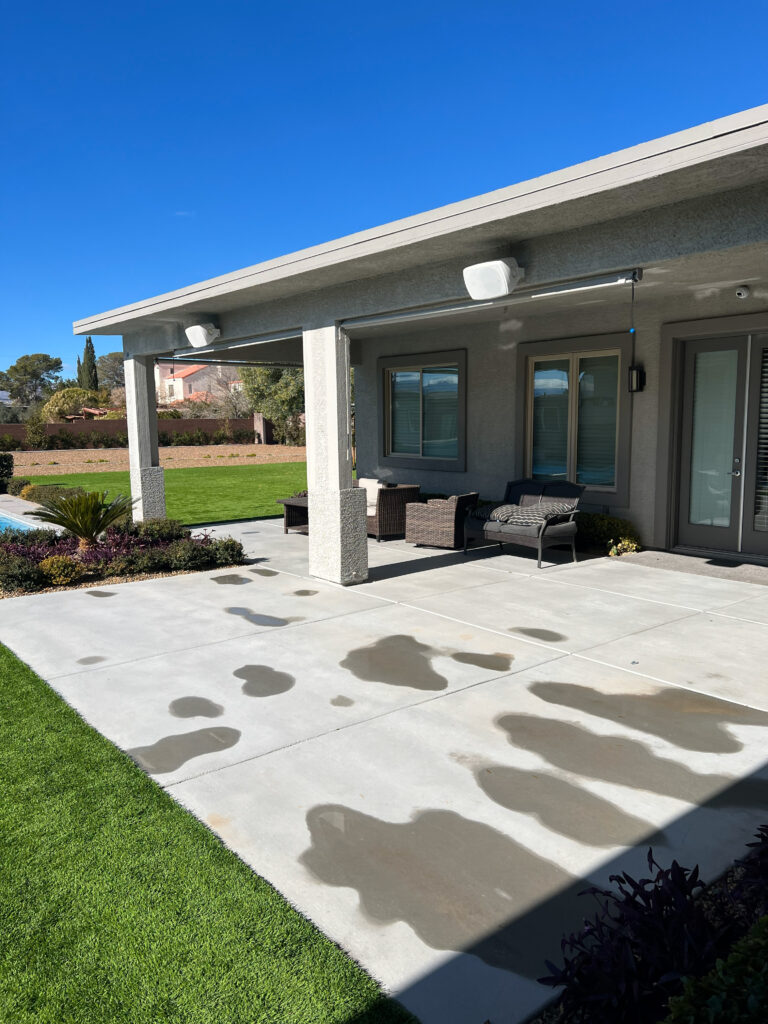 Covered patio with modern seating, showcasing concrete with water spots and a sunny, blue sky. Ideal for outdoor relaxation and gatherings.