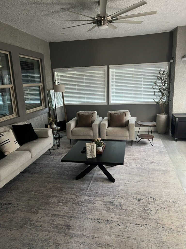 Bright and modern lounge area featuring two armchairs and a light sofa around a black coffee table. Large windows provide natural light.