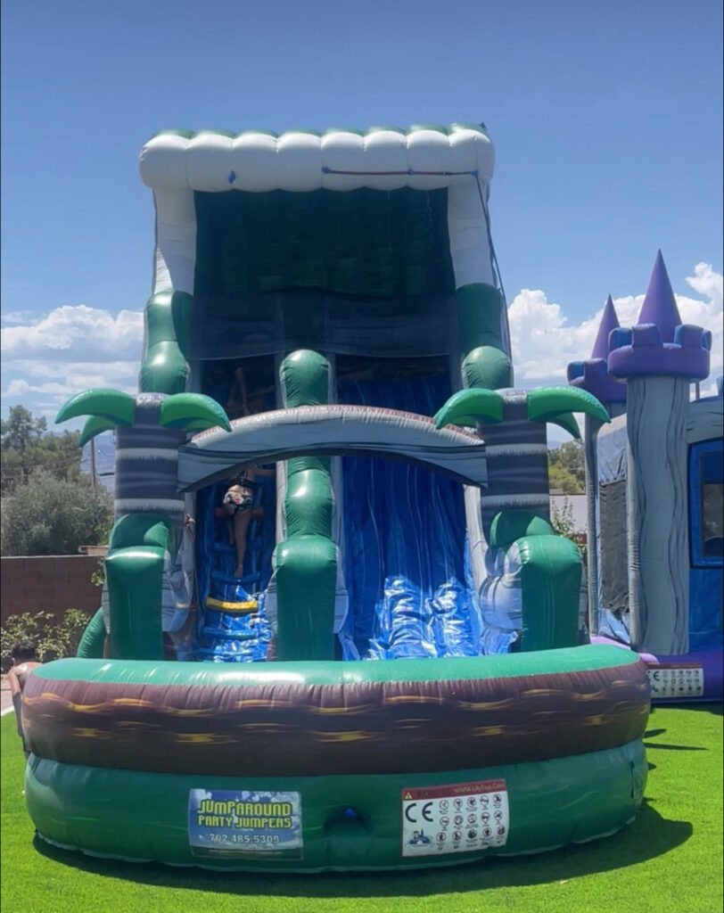 Colorful inflatable water slide with a palm tree design, featuring a child sliding down. Ideal for summer parties and outdoor fun.
