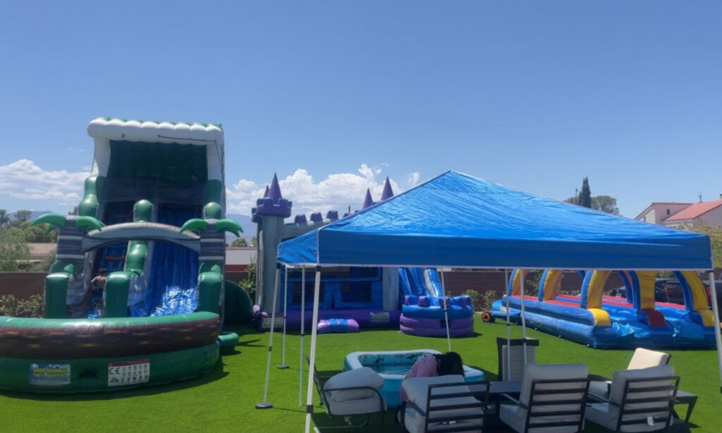 Colorful inflatable water slide, castle, and obstacle course under a blue tent on green grass, perfect for outdoor summer parties.