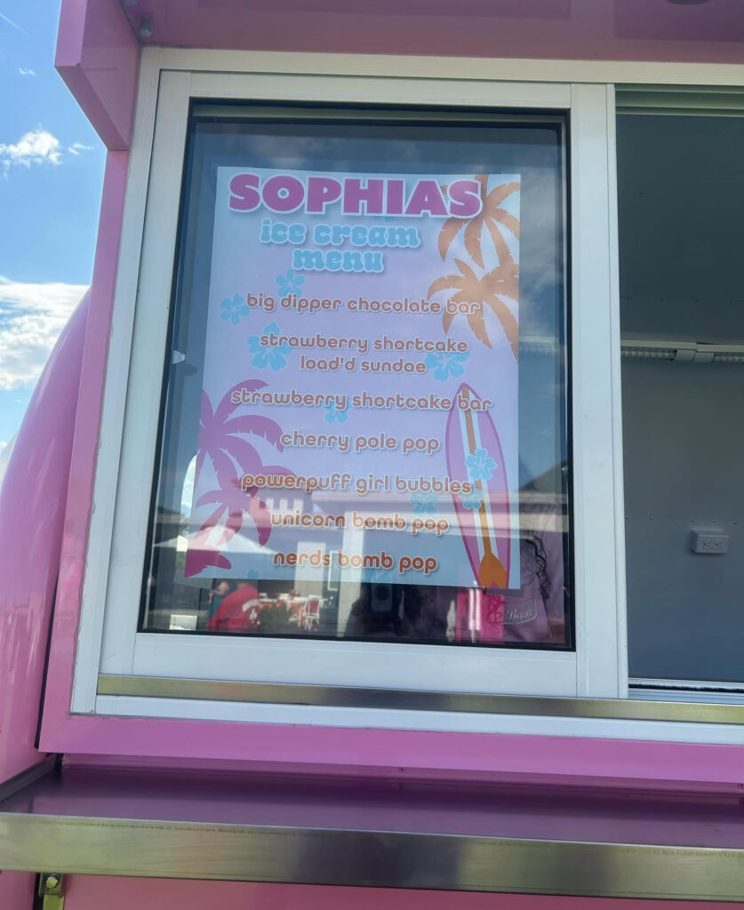 Colorful ice cream menu at Sophia's stand lists treats like Strawberry Shortcake Sundae and Powerpuff Girl Bubbles, enticing visitors on a sunny day.