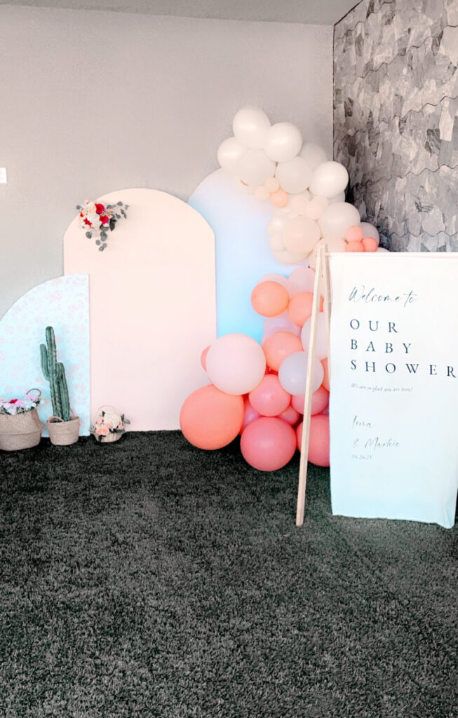 Decorative setup for a baby shower, featuring colorful balloons, floral accents, and a welcome sign with the event details.