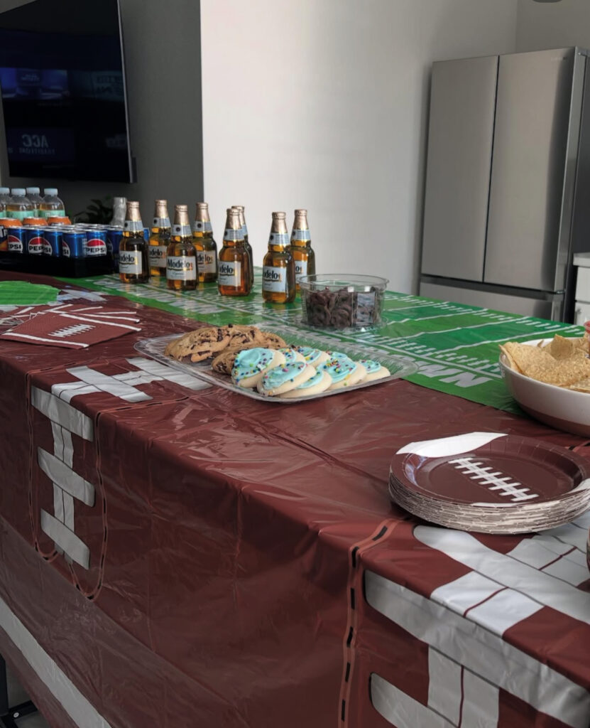 A festive table set for a game day, featuring snacks like cookies, chips, and drinks, with a football-themed tablecloth.
